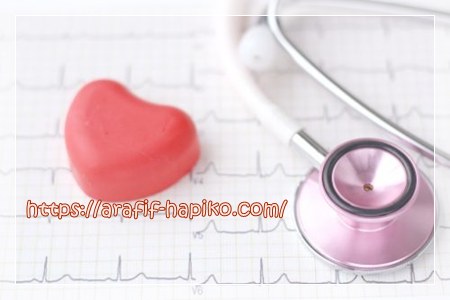 聴診器と心電図の上に置かれた赤いハートのオブジェ。